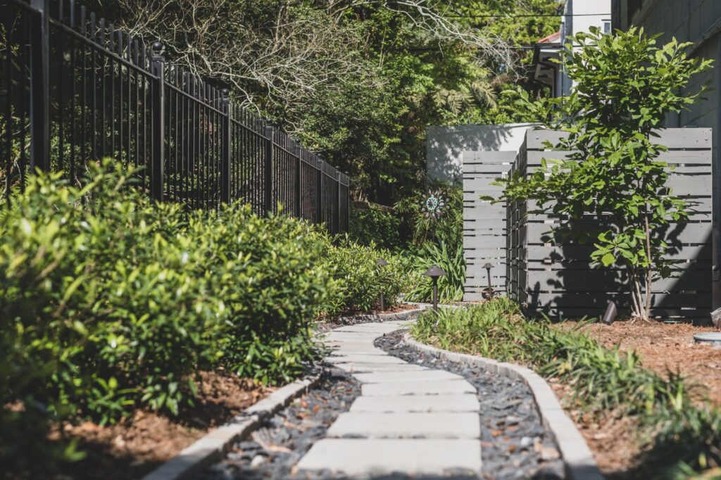 Image of a renovated backyard with pavers, bushes, and a custom trellis, completed by Miller Outdoors, a New Orleans Landscape Designer.