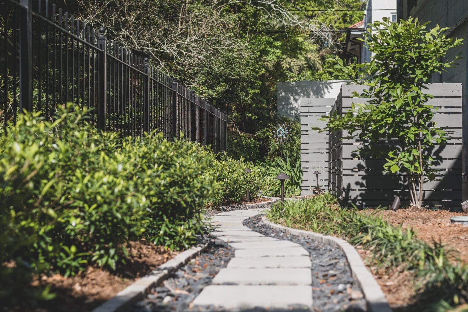 Image of a renovated backyard with pavers, bushes, and a custom trellis, completed by Miller Outdoors, a New Orleans Landscape Designer.