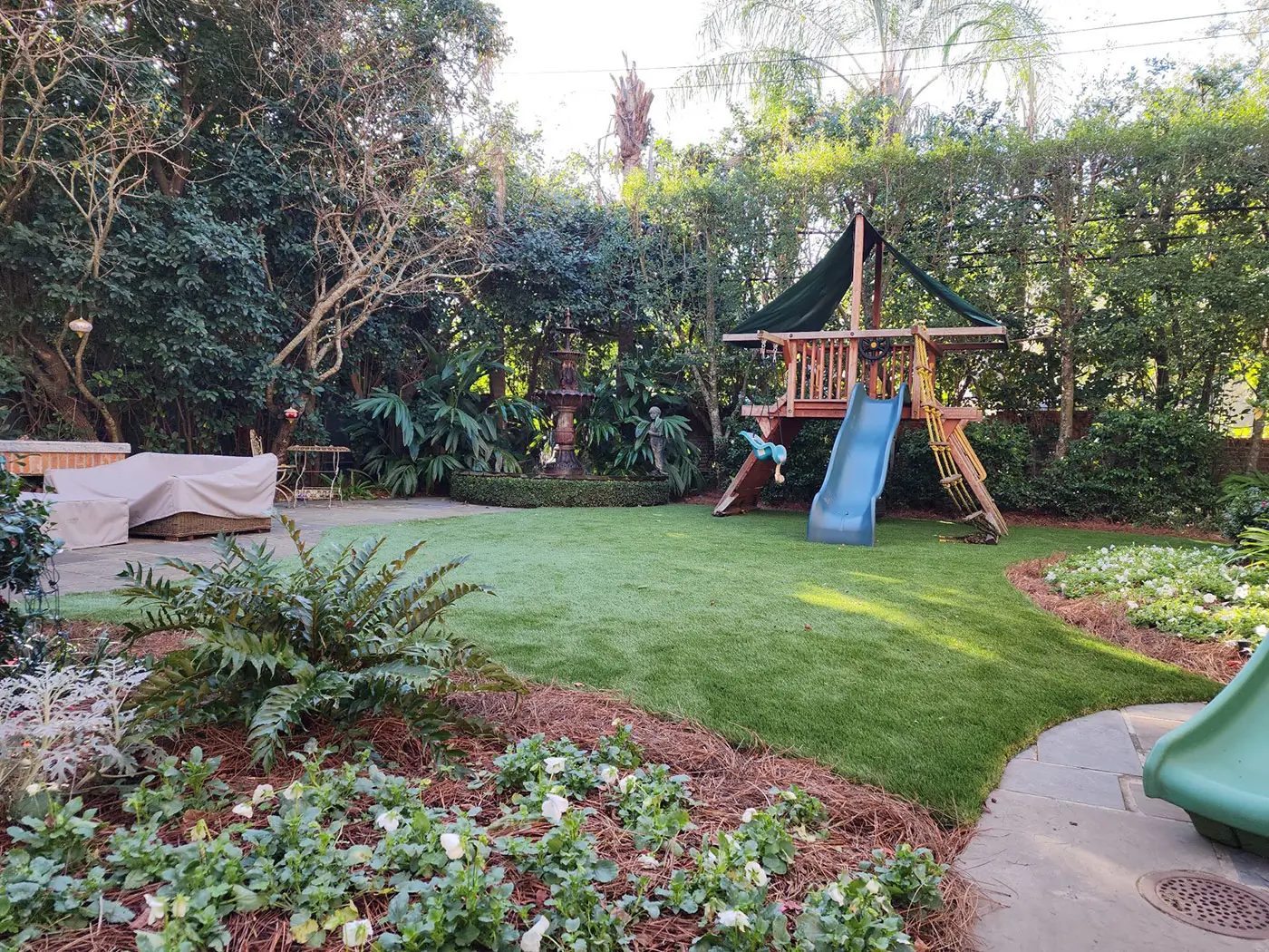An image of a small backyard with a children's playset and a fountain for the blog "How Miller Outdoors NOLA Masters New Orleans Landscape Design for Small Homes"