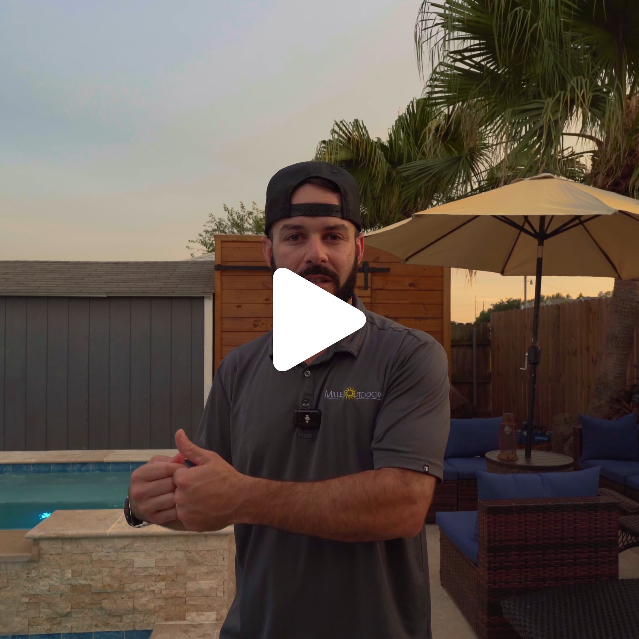 A man with a beard and backwards cap stands by a backyard pool, outdoor furniture, and umbrella, gesturing with his hands—perfect for a summer blog. A fence and palm tree frame the scene, with a play button centered on the image.